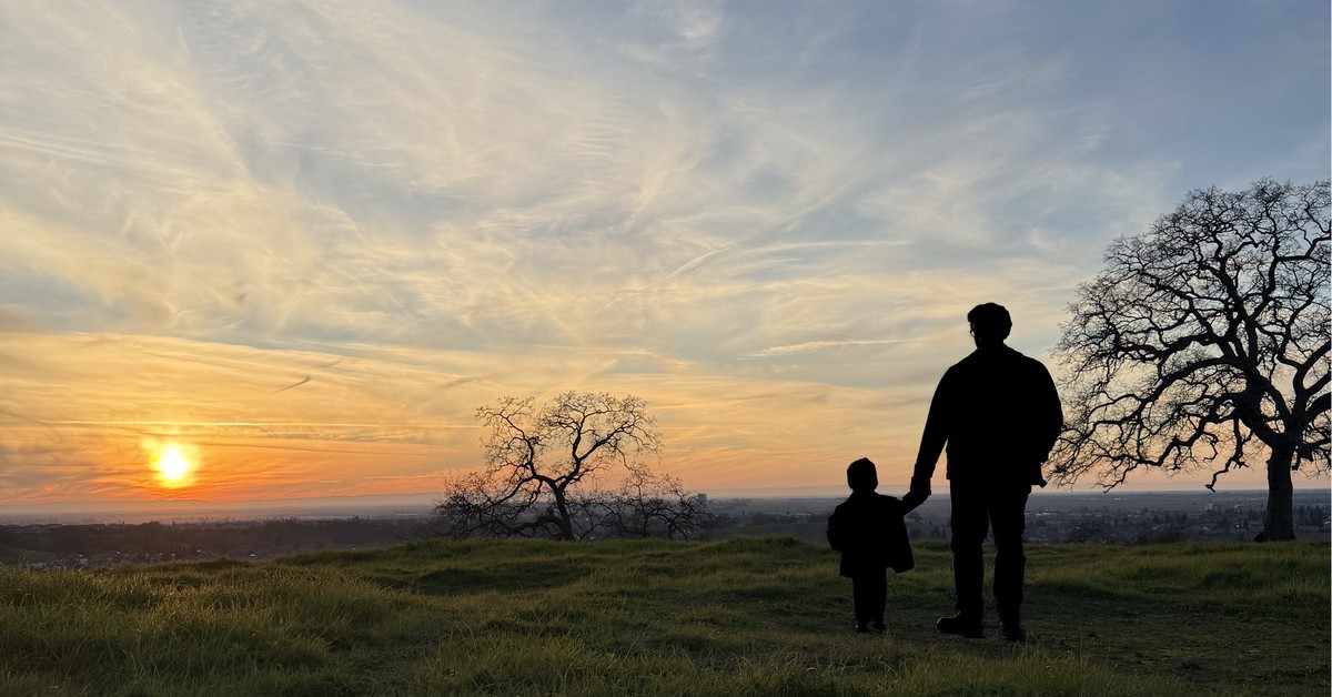 Silhouette of a parent and child watching the sunset over California hills